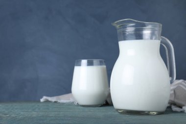 Mavi arka planda, tahta masanın üzerinde taze süt bulunan sürahi ve bardak. Metin için boşluk