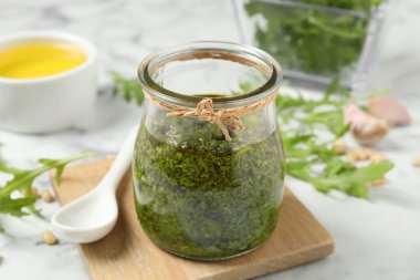 Lezzetli roka pesto kavanozu ve beyaz masa malzemeleri.