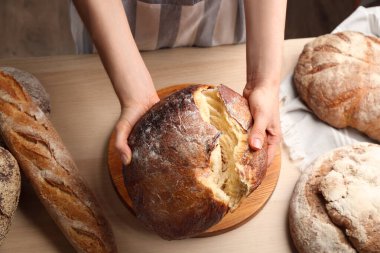 Ahşap masada yeni pişmiş ekmeği kıran kadın, yakın plan.