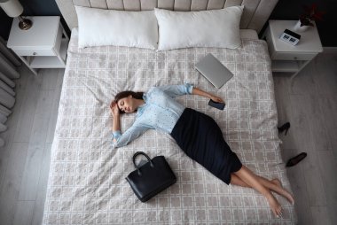 Exhausted businesswoman in office wear sleeping on bed at home after work, above view clipart