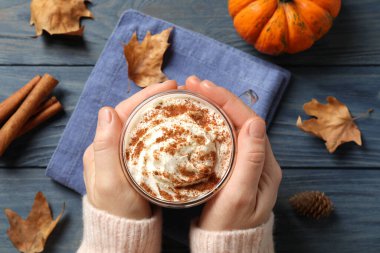 Mavi ahşap masada nefis balkabaklı latte tutan bir kadın.
