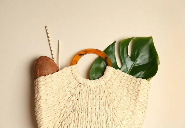 Elegant woman\'s straw bag with coconut, tropical leaf and straws on beige background, top view