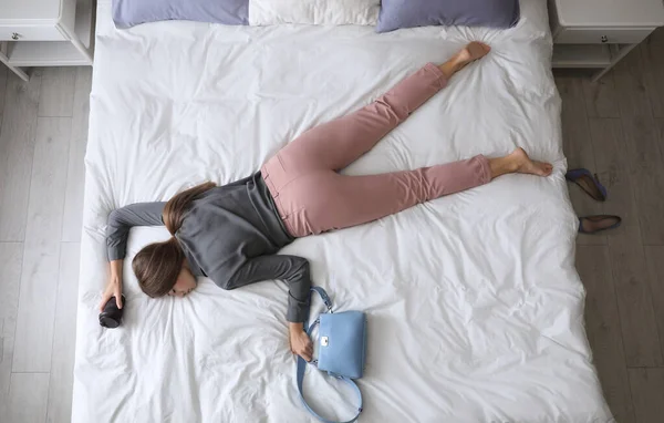 Exhausted woman with cup of coffee and purse sleeping fully dressed on bed at home, above view