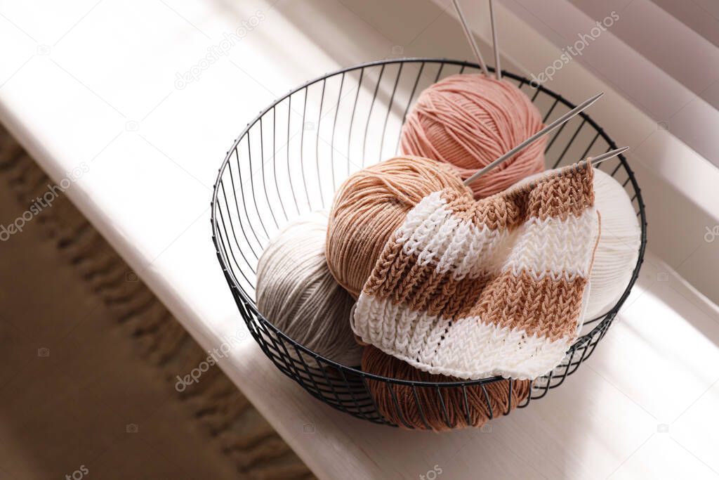 Yarn balls and knitting needles in metal basket on window sill indoors. Creative hobby