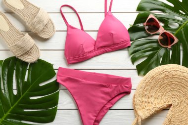 Güzel pembe bikini ve beyaz ahşap arka planda plaj aksesuarları.