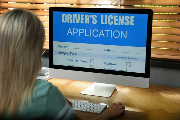 Woman using computer to fill driver\'s license application form at table in office, closeup