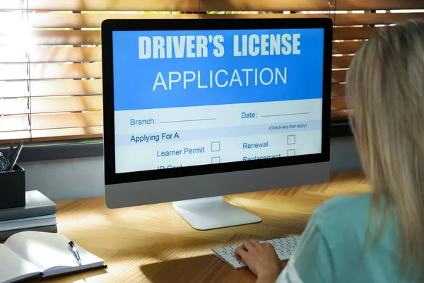 Woman using computer to fill driver\'s license application form at table in office, closeup