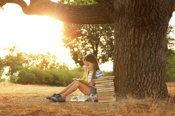 Cute little girl reading book near tree in park