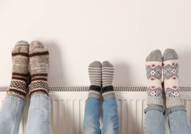 Beyaz duvarın yanındaki ısıtma kaloriferinde aile ısınma bacakları, yakın plan.