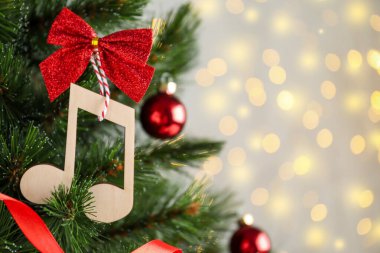 Tahta bir nota ve kırmızı bir fiyonk, bulanık ışıklara karşı Noel ağacında asılı. Metin için boşluk