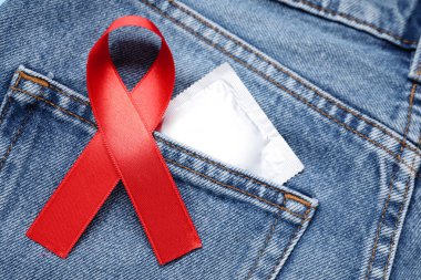 Kırmızı kurdeleli ve prezervatifli kotlar, yakın plan. AIDS Hastalığı Farkındalığı
