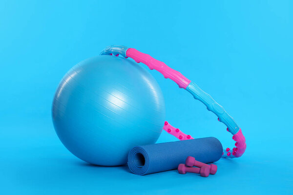 Hula hoop, exercise ball, yoga mat and dumbbells on light blue background