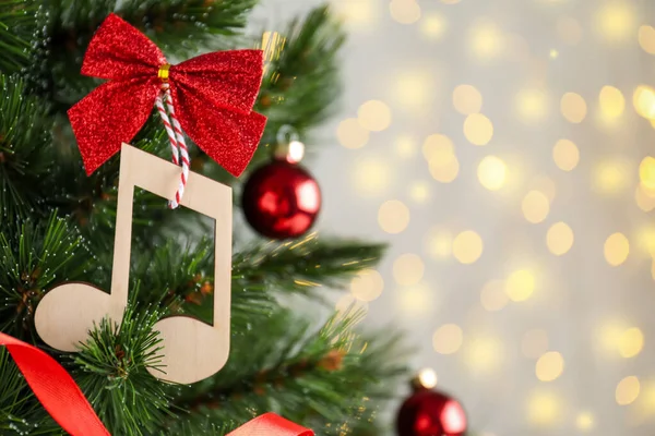 赤い弓がぼやけた光に対してクリスマスツリーにぶら下がっている木製の音楽ノート テキストのスペース — ストック写真
