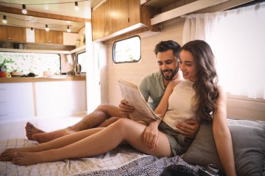 Karavanda yatakta gazete okuyan mutlu genç çift. Kamp tatili