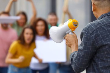Protesto lideri megafonla dışarıda kalabalıkla konuşuyor.