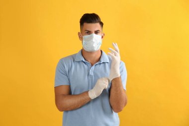 Koruyucu maskeli adam sarı arka planda tıbbi eldiven takıyor.