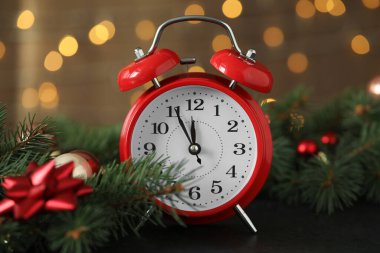 Siyah masanın üzerindeki desenli çalar saat bulanık Noel ışıklarına karşı, yakın plan. Yeni yıl geri sayımı
