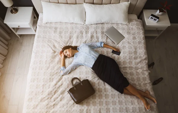 Exhausted businesswoman in office wear sleeping on bed at home after work, above view