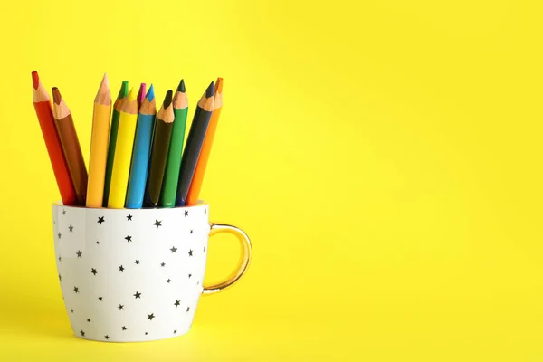 Colorful pencils in cup on yellow background. Space for text