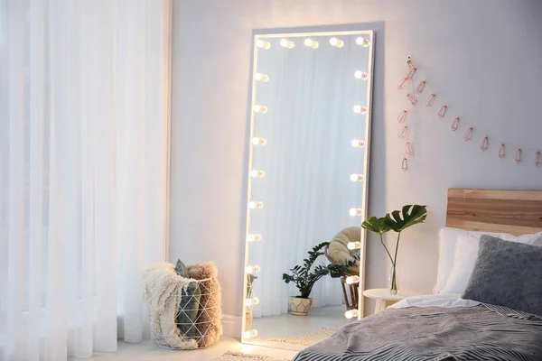 Full length dressing mirror with lamps in stylish bedroom interior