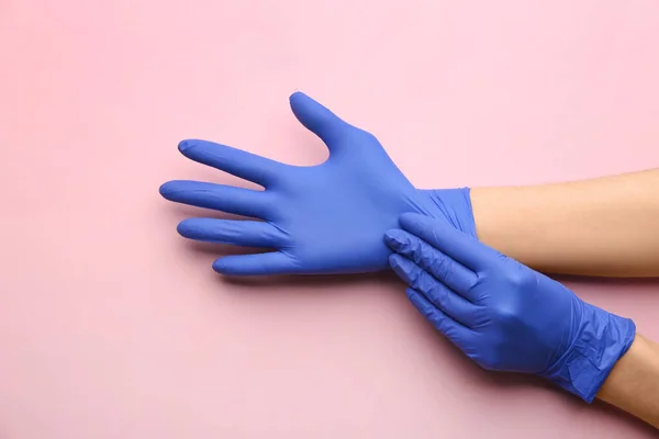 Person putting on medical gloves against pink background, closeup of hands