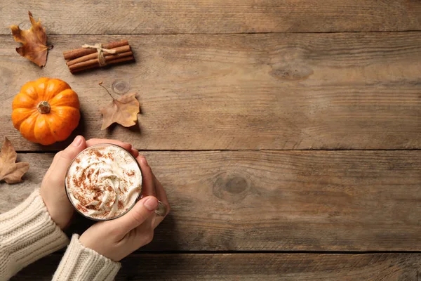 Woman holding tasty pumpkin latte at wooden table, top view. Space for text