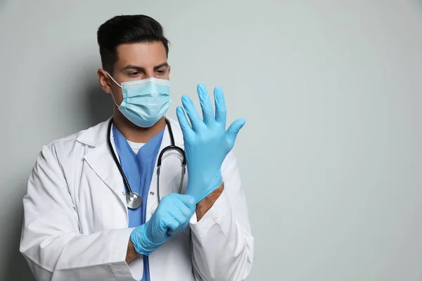 Doctor Beschermende Masker Zetten Medische Handschoenen Tegen Lichtgrijze Achtergrond — Stockfoto