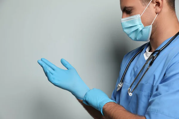 Doctor Beschermende Masker Zetten Medische Handschoenen Tegen Lichtgrijze Achtergrond — Stockfoto