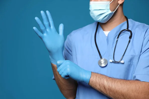 Dokter Beschermende Masker Zetten Medische Handschoenen Tegen Blauwe Achtergrond Close — Stockfoto