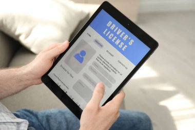 Evde elinde ehliyet başvuru formu olan tablet tutan bir adam var.