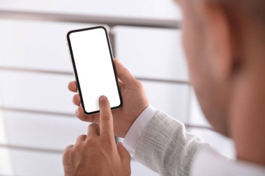 Kapalı alanda boş ekranlı cep telefonu kullanan bir adam.