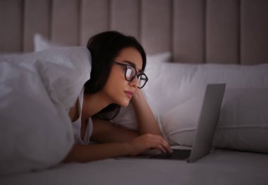 Gece yatağında dizüstü bilgisayar kullanan, nomofobisi olan genç bir kadın. Uykusuzluk kavramı