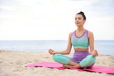 Plajda yoga yapan genç bir kadın, mesaj atmak için yer var. Vücut eğitimi