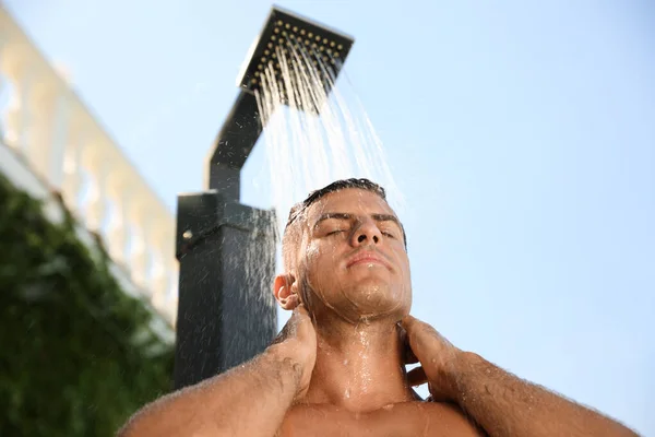 Man washing hair in outdoor shower on summer day