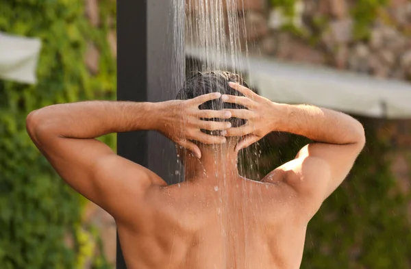 Man washing hair in outdoor shower on summer day