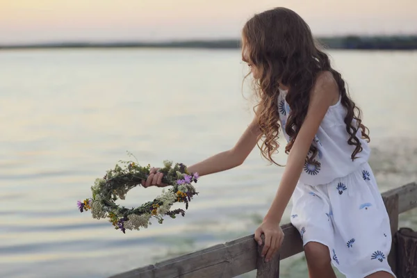 かわいい女の子は夜に川の近くに美しい花で作られた花輪を保持 — ストック写真
