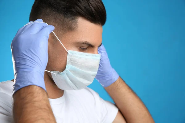 Hombre Con Guantes Médicos Poniéndose Mascarilla Protectora Contra Fondo Azul — Foto de Stock