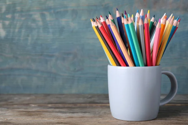 Colorful pencils in cup on wooden table. Space for text