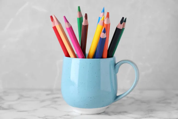 Colorful pencils in cup on white marble table against grey background