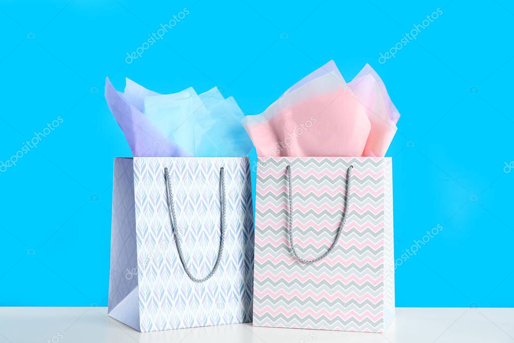 Gift bags with paper on white table against light blue background