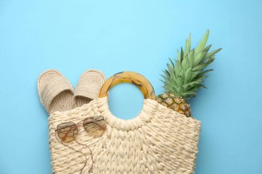 Ayakkabılı, güneş gözlüklü ve açık mavi arka planda ananaslı zarif bir kadın saman çantası.