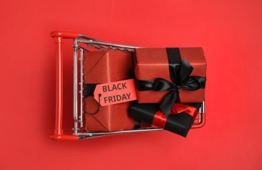 Kırmızı arka planda hediye paketleri olan küçük alışveriş arabası, üst manzara. Kara Cuma indirimi