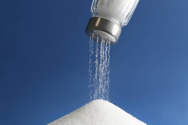 Pouring salt from shaker on blue background, closeup