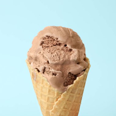 Açık mavi arka planda waffle külahlı lezzetli çikolatalı dondurma, yakın plan.