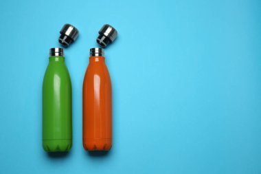 Açık mavi arka planda modern termo şişeler, düz konum. Metin için boşluk