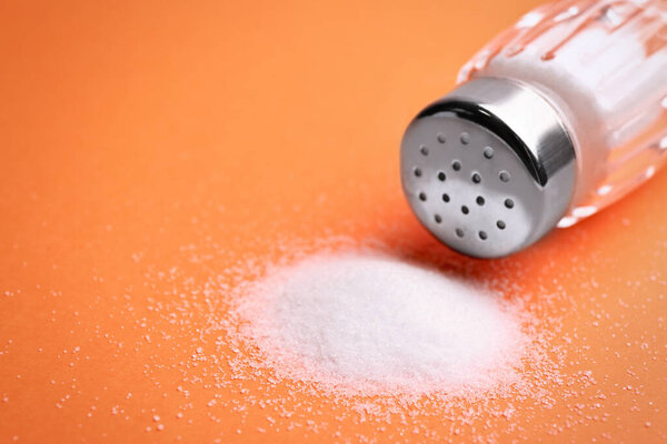 Scattered salt and shaker on orange background, closeup. Space for text