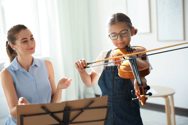 Young woman teaching little girl to play violin indoors