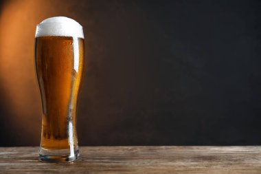 Koyu arka planda, ahşap masada soğuk, lezzetli bir bira. Metin için boşluk