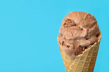 Açık mavi arka planda waffle külahlı lezzetli çikolatalı dondurma, yakın plan. Metin için boşluk