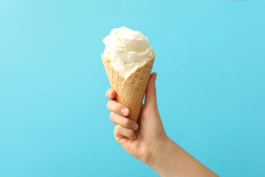 Açık mavi arka planda nefis dondurmalı waffle külahı tutan kadın, yakın plan.